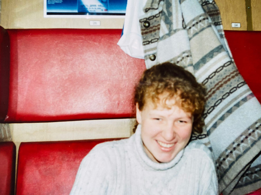 Nadine lachend in einem Zugabteil mit rotem Leder