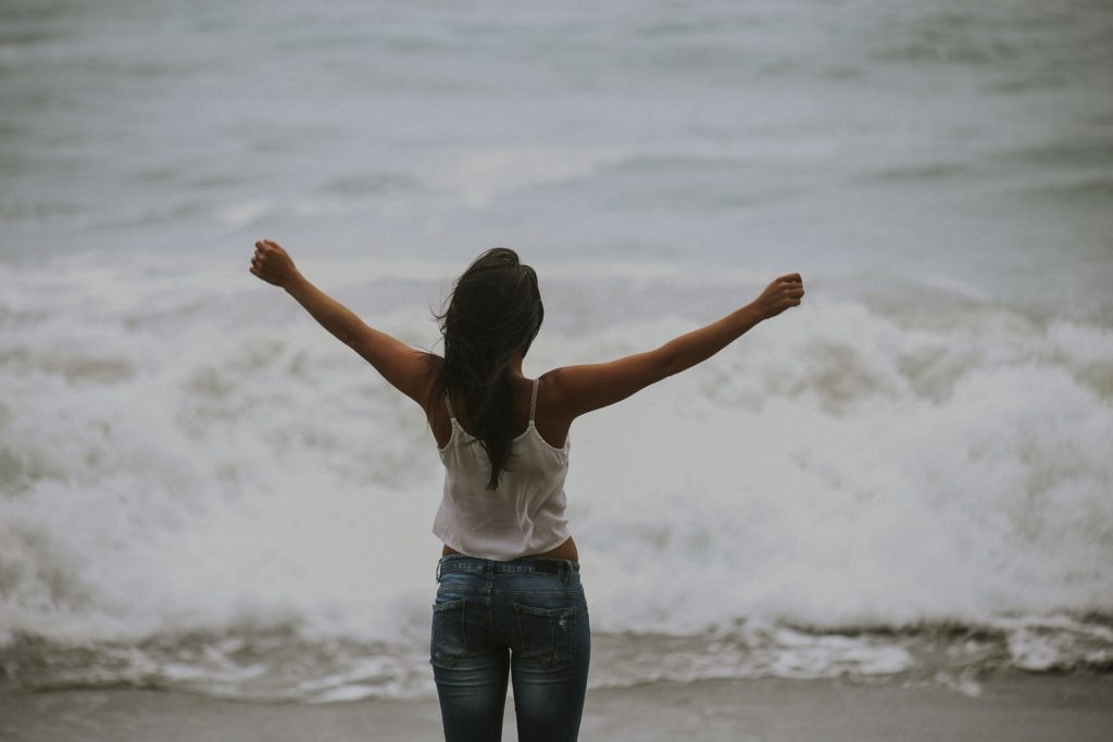 Eine Frau steht am Meer und genießt die Wellen und die Freiheit. 